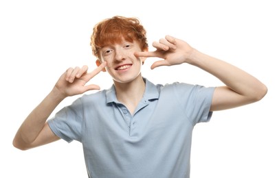 Smiling teenage boy pointing at his freckles on white background