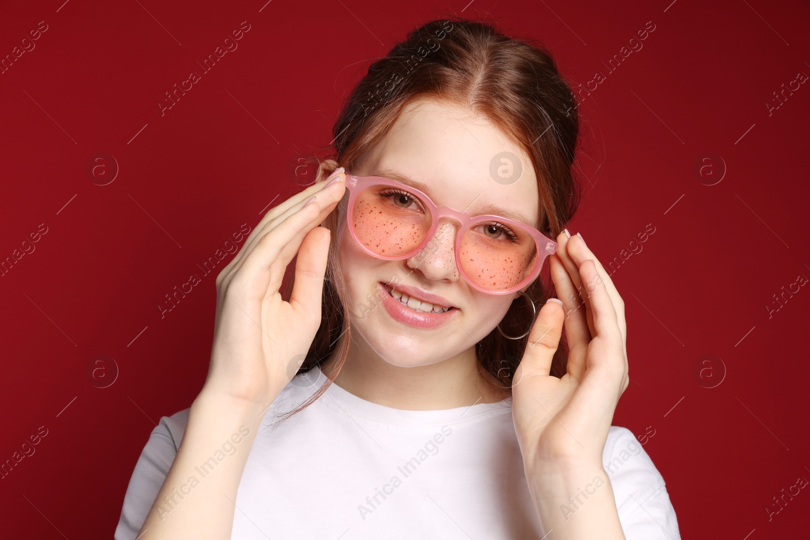 Photo of Beautiful freckled teenage girl with sunglasses on red background