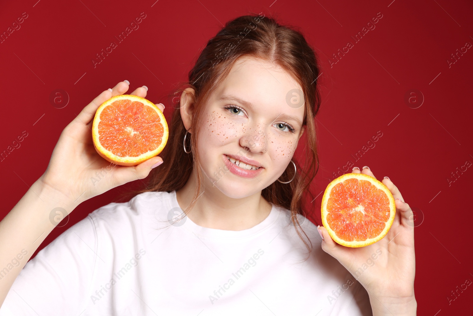 Photo of Beautiful teenage girl with freckles holding grapefruit slices on red background