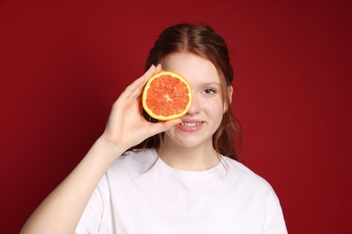 Photo of Beautiful teenage girl with freckles holding grapefruit slice on red background