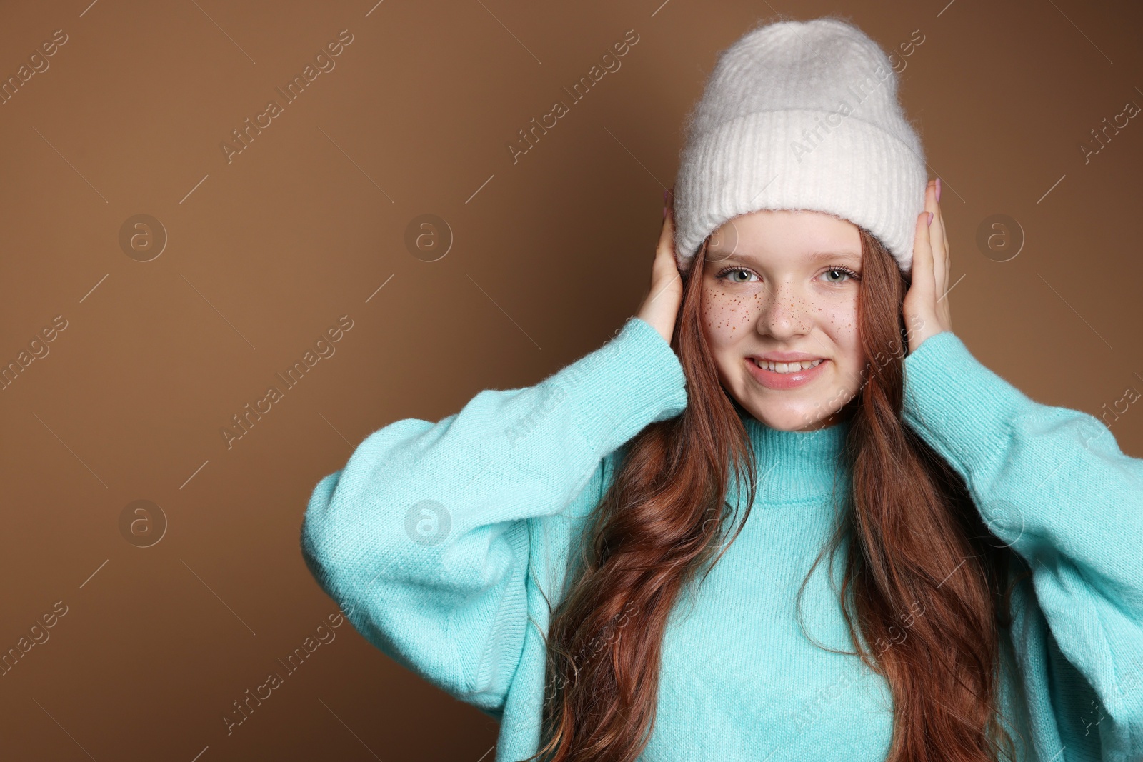 Photo of Beautiful teenage girl with freckles in hat on brown background, space for text