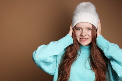 Photo of Beautiful teenage girl with freckles in hat on brown background, space for text