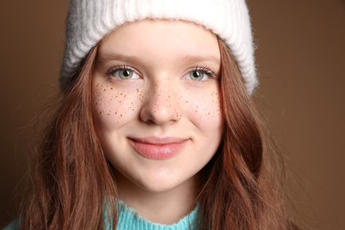 Beautiful teenage girl with freckles in hat on brown background, closeup