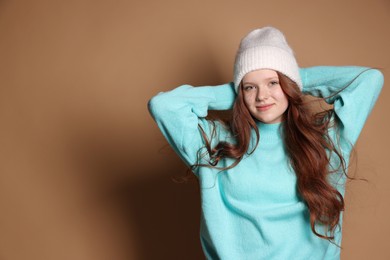 Beautiful teenage girl with freckles in hat on brown background, space for text