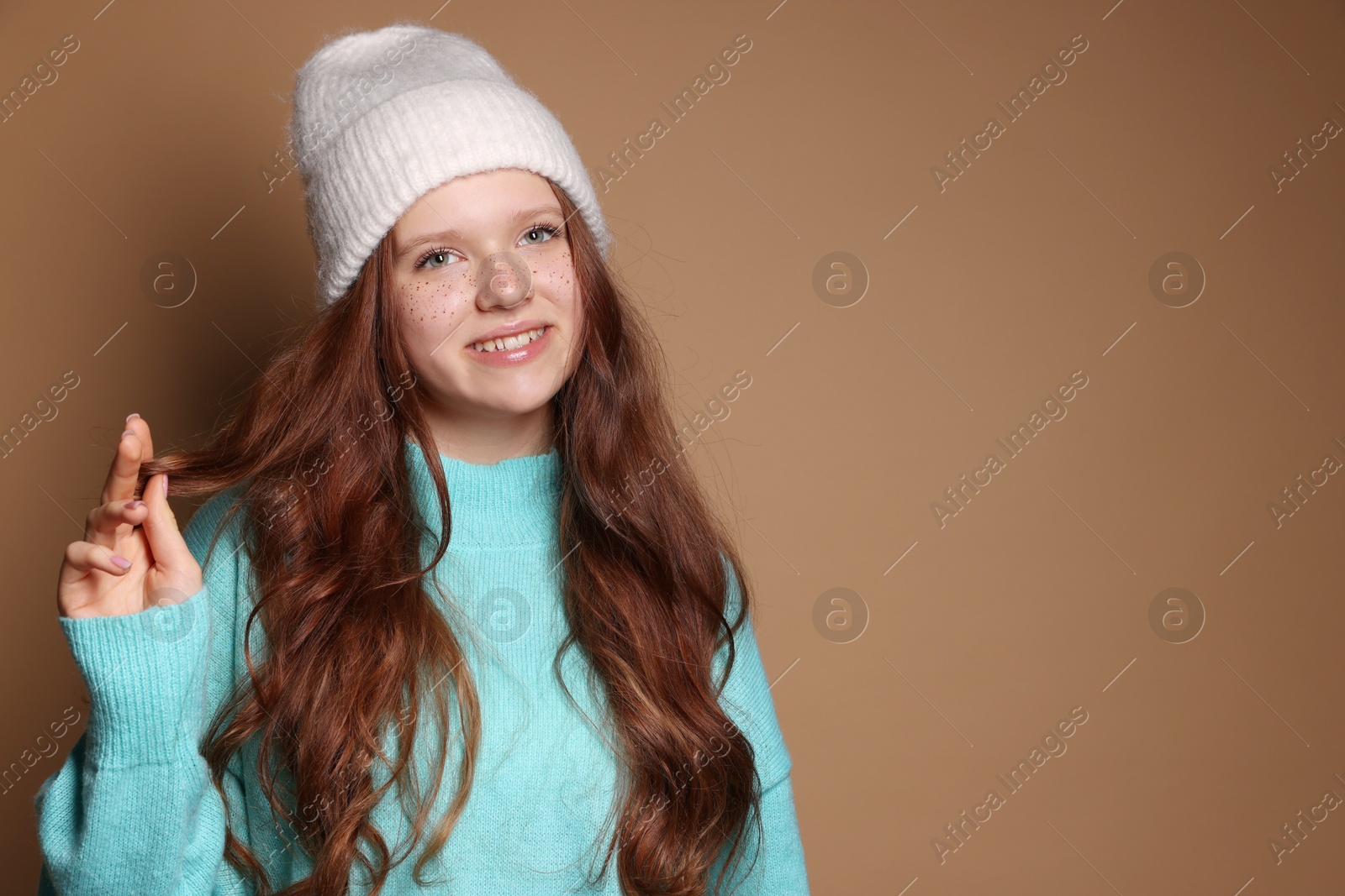 Photo of Beautiful teenage girl with freckles in hat on brown background, space for text