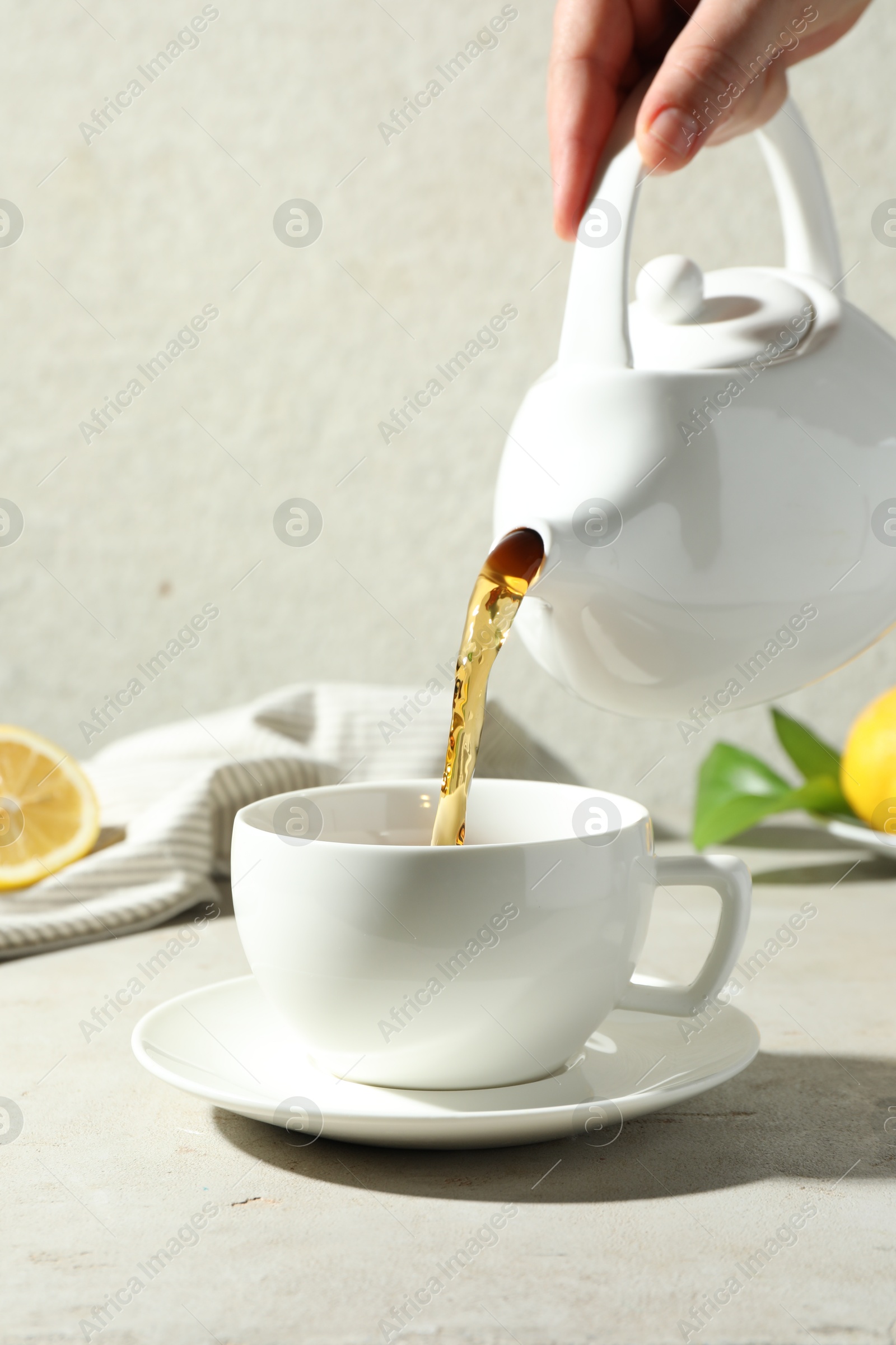 Woman pouring aromatic tea from teapot into cup at light textured table, closeup Photo of Woman pouring aromatic tea from teapot into cup at light textured table, closeup