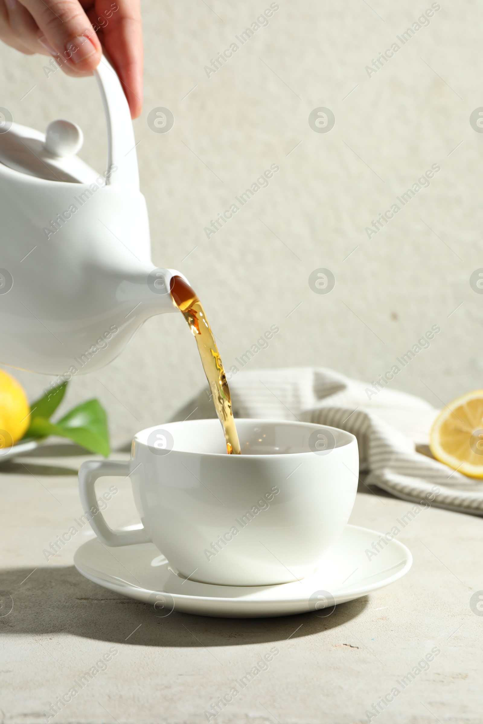 Woman pouring aromatic tea from teapot into cup at light textured table, closeup Photo of Woman pouring aromatic tea from teapot into cup at light textured table, closeup