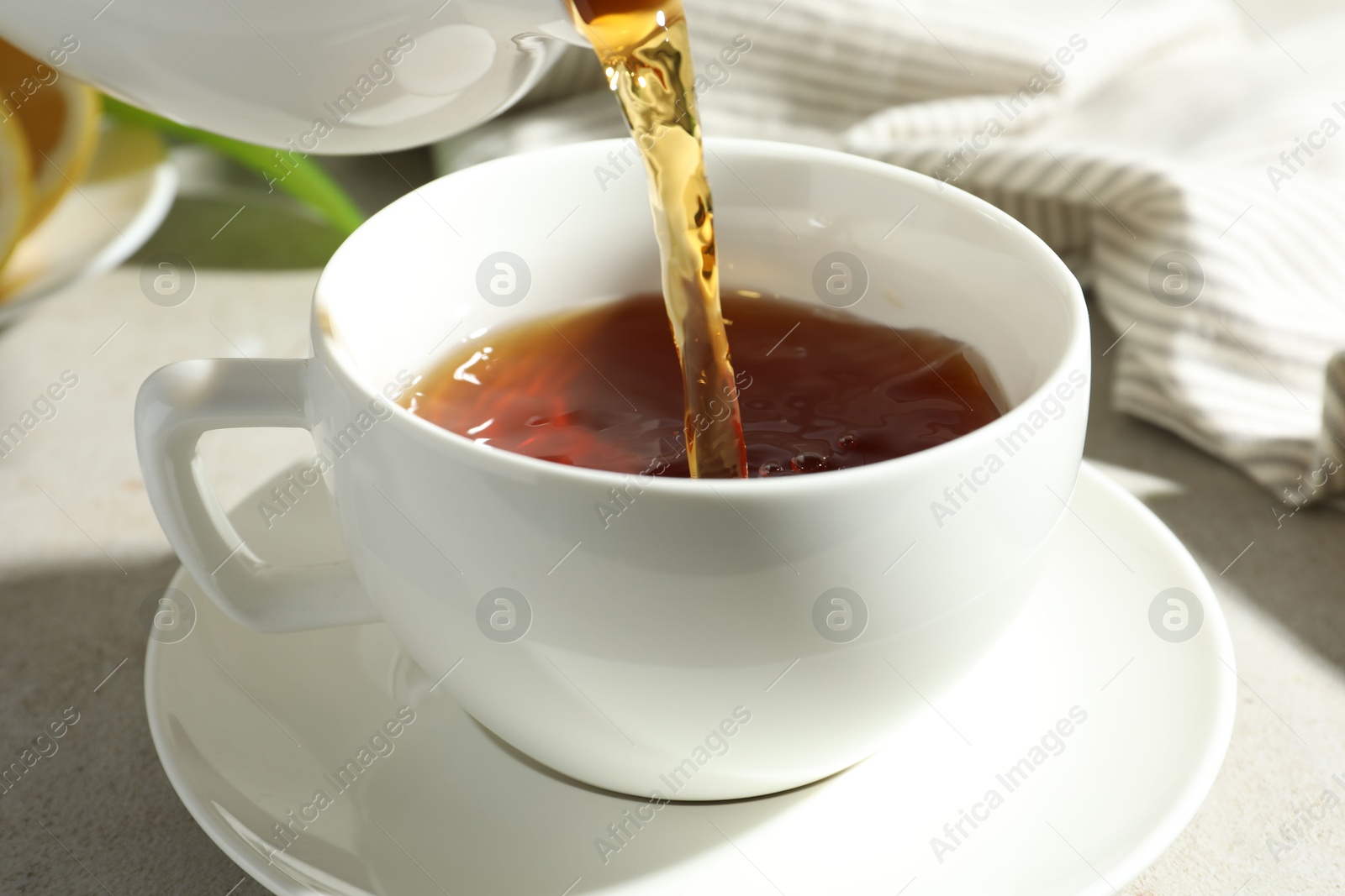 Pouring aromatic tea from teapot into cup at light textured table, closeup Photo of Pouring aromatic tea from teapot into cup at light textured table, closeup
