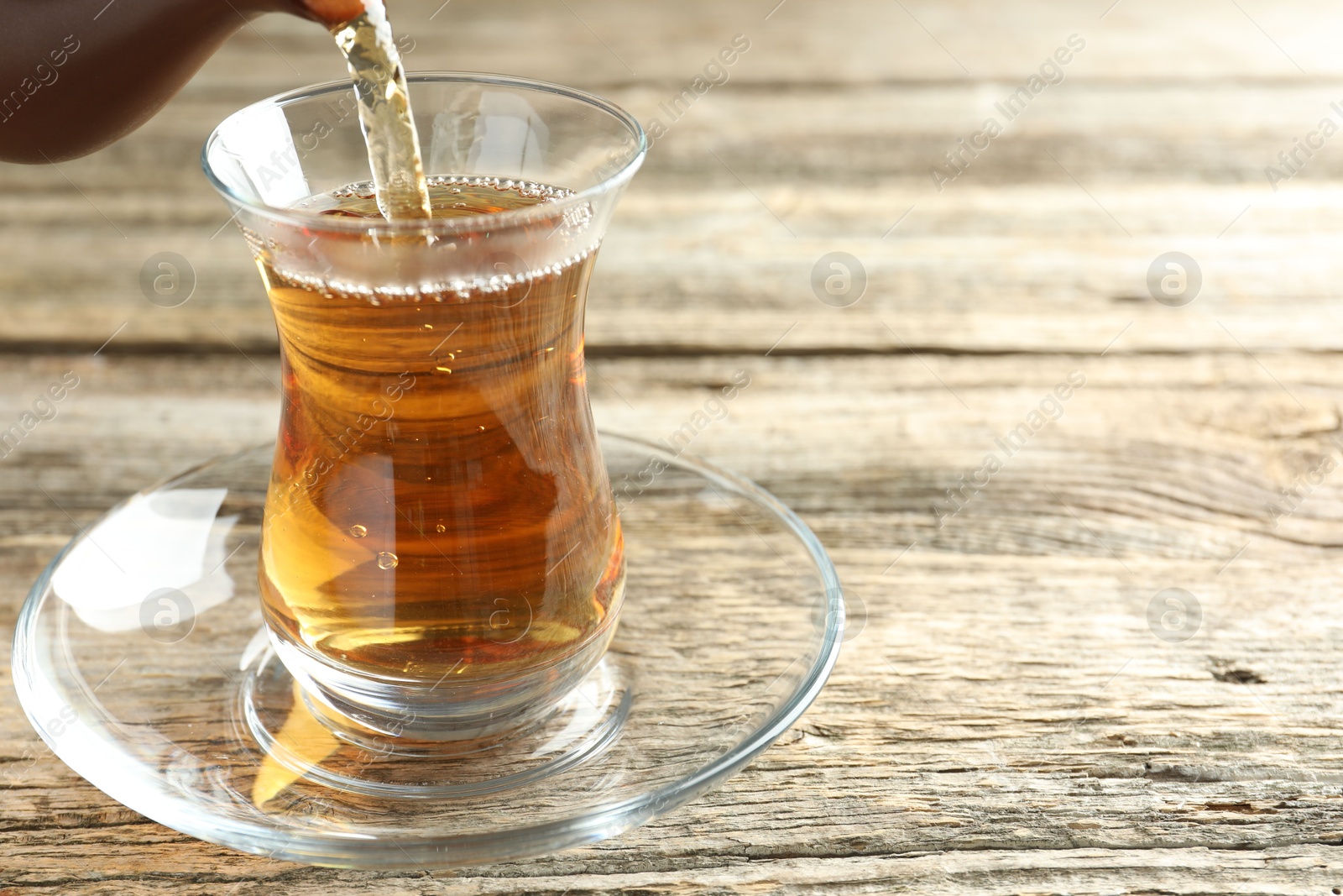 Pouring aromatic tea into glass at wooden table, closeup. Space for text Photo of Pouring aromatic tea into glass at wooden table, closeup. Space for text