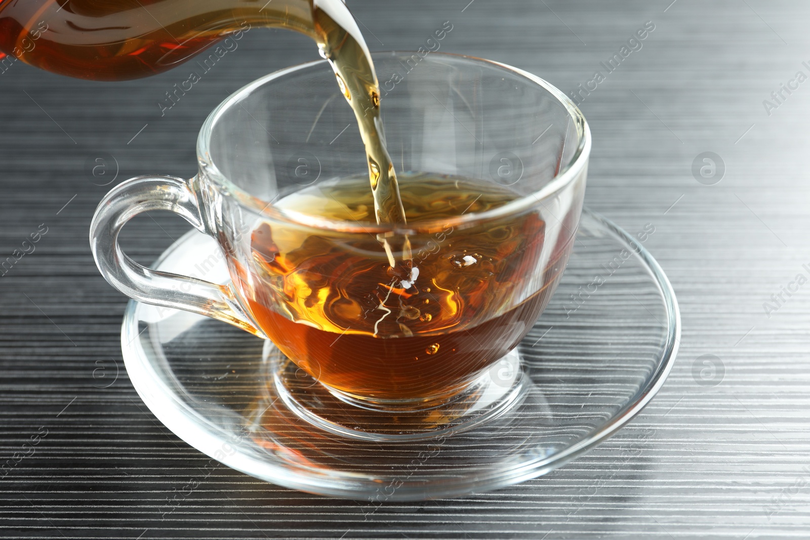 Pouring aromatic tea into cup at black wooden table, closeup Photo of Pouring aromatic tea into cup at black wooden table, closeup