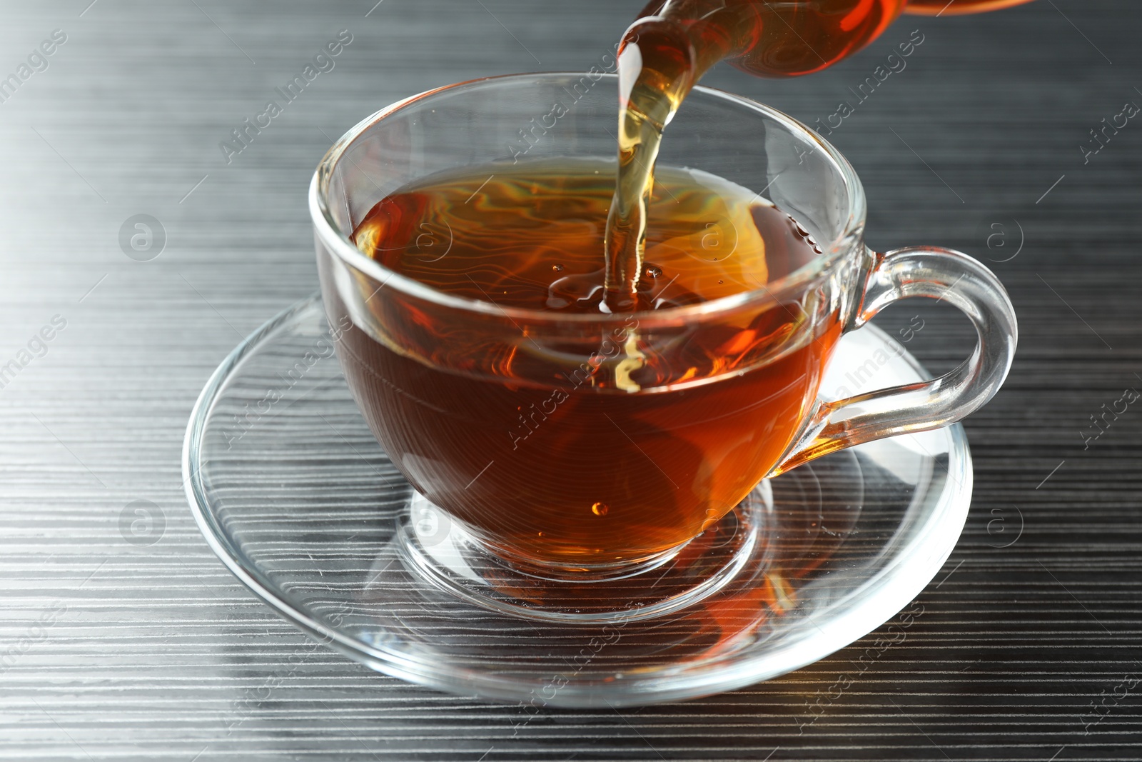 Pouring aromatic tea into cup at black wooden table, closeup Photo of Pouring aromatic tea into cup at black wooden table, closeup