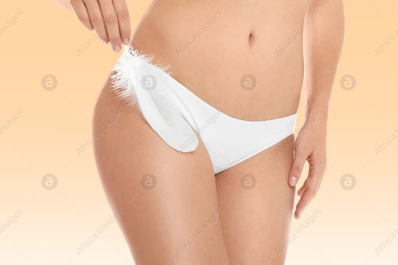 Image of Woman with feather showing smooth skin on peach color background, closeup. Bikini epilation