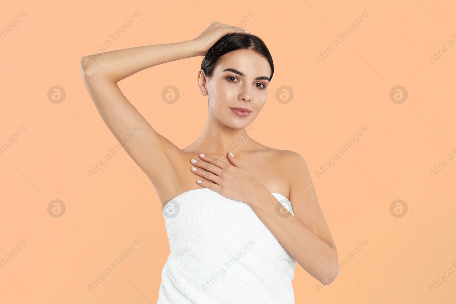 Image of Young woman showing hairless armpit after epilation procedure on peach color background