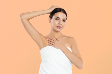 Young woman showing hairless armpit after epilation procedure on peach color background