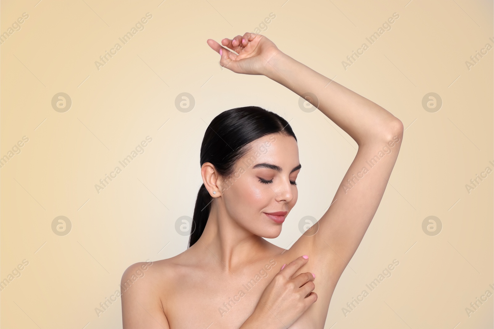 Image of Young woman showing hairless armpit after epilation procedure on dark beige background