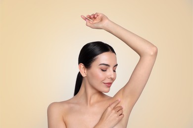 Young woman showing hairless armpit after epilation procedure on dark beige background