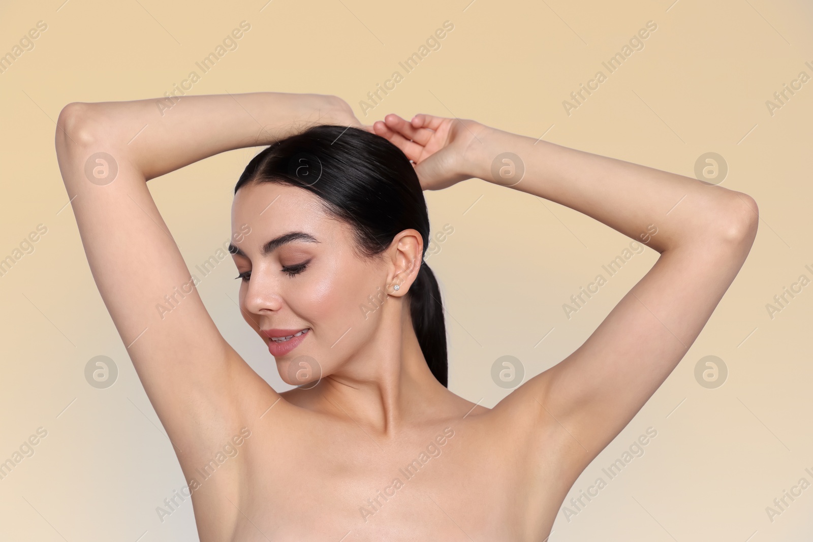 Image of Young woman showing hairless armpit after epilation procedure on dark beige background