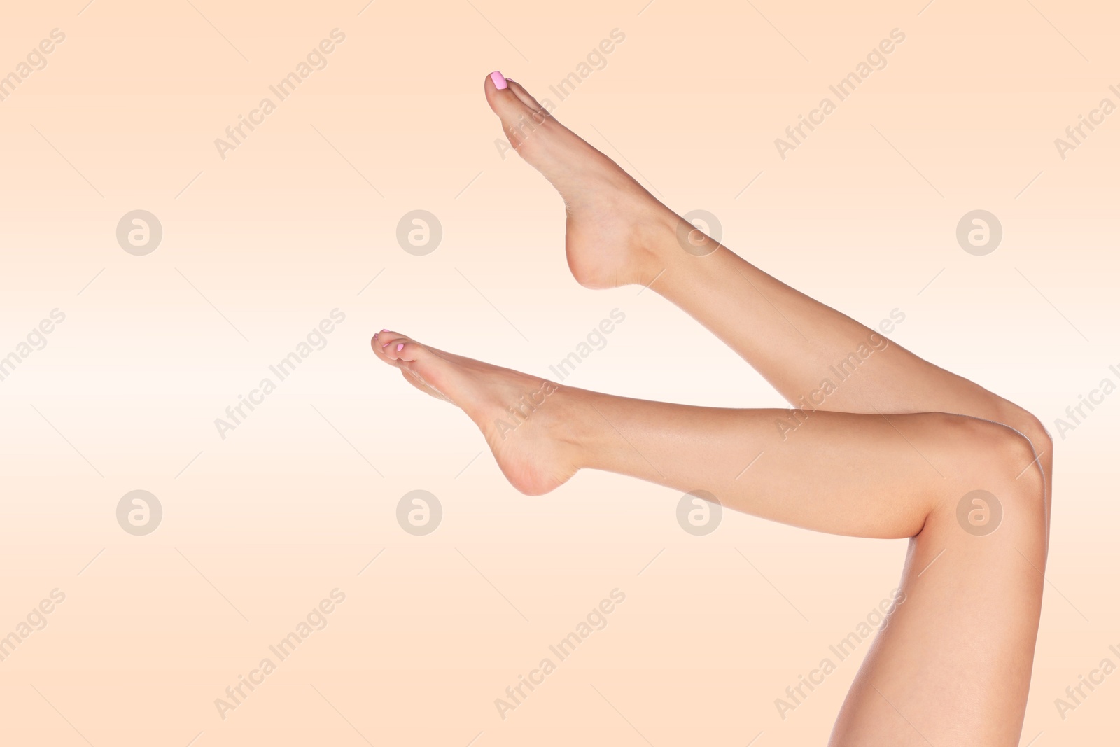 Image of Young woman showing legs with smooth skin after epilation procedure on pink beige background, closeup