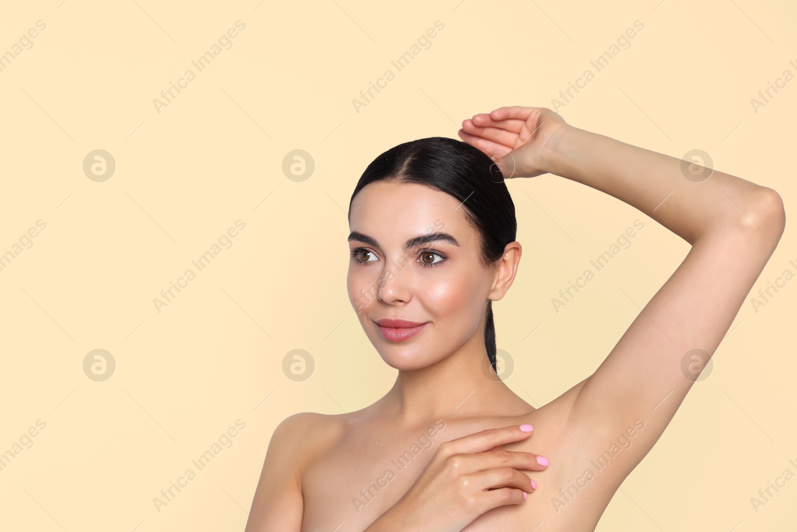 Image of Young woman showing hairless armpit after epilation procedure on dark beige background. Space for text