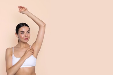 Young woman showing hairless armpit after epilation procedure on pink beige background. Space for text