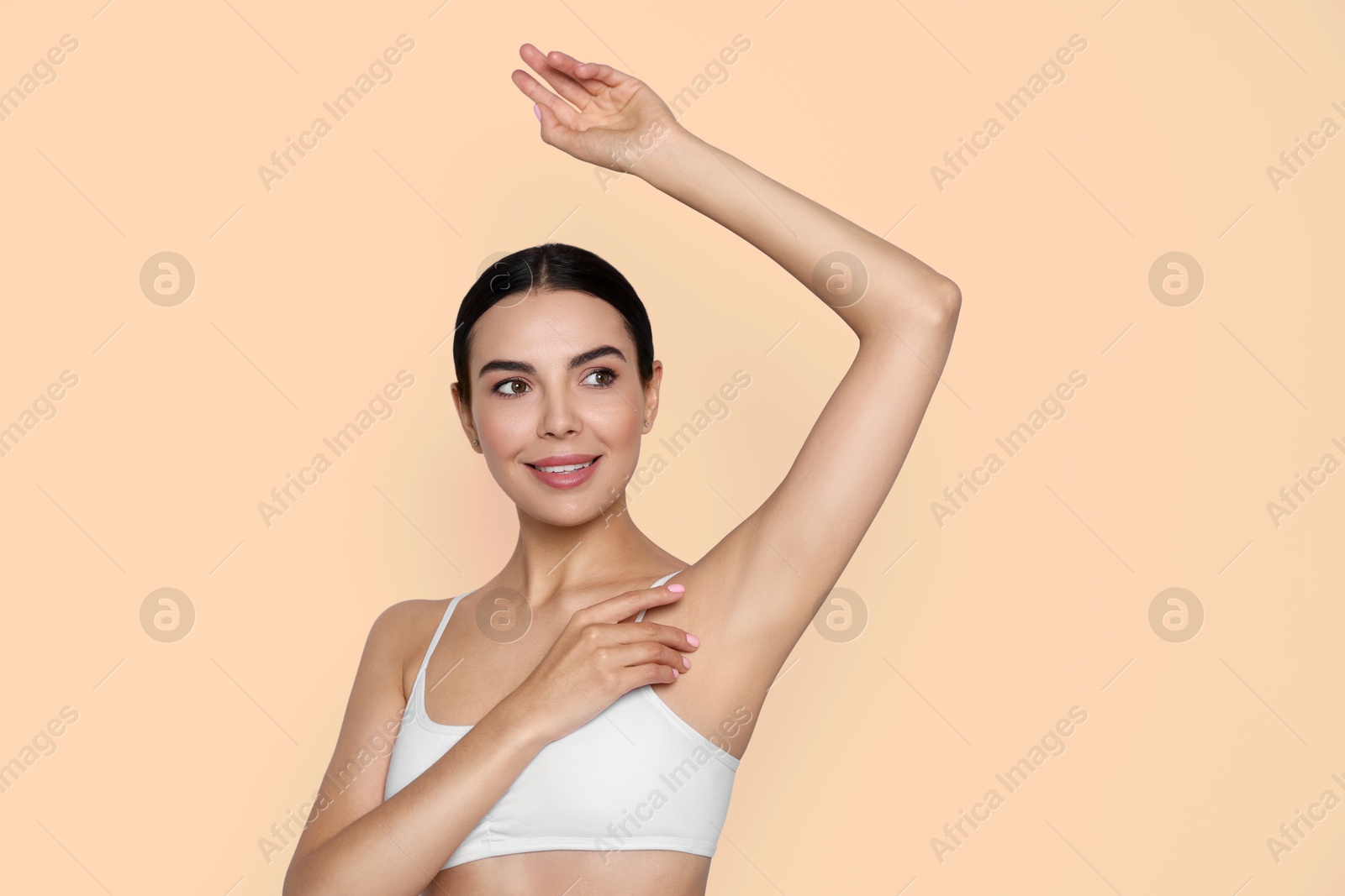 Image of Young woman showing hairless armpit after epilation procedure on dark beige background