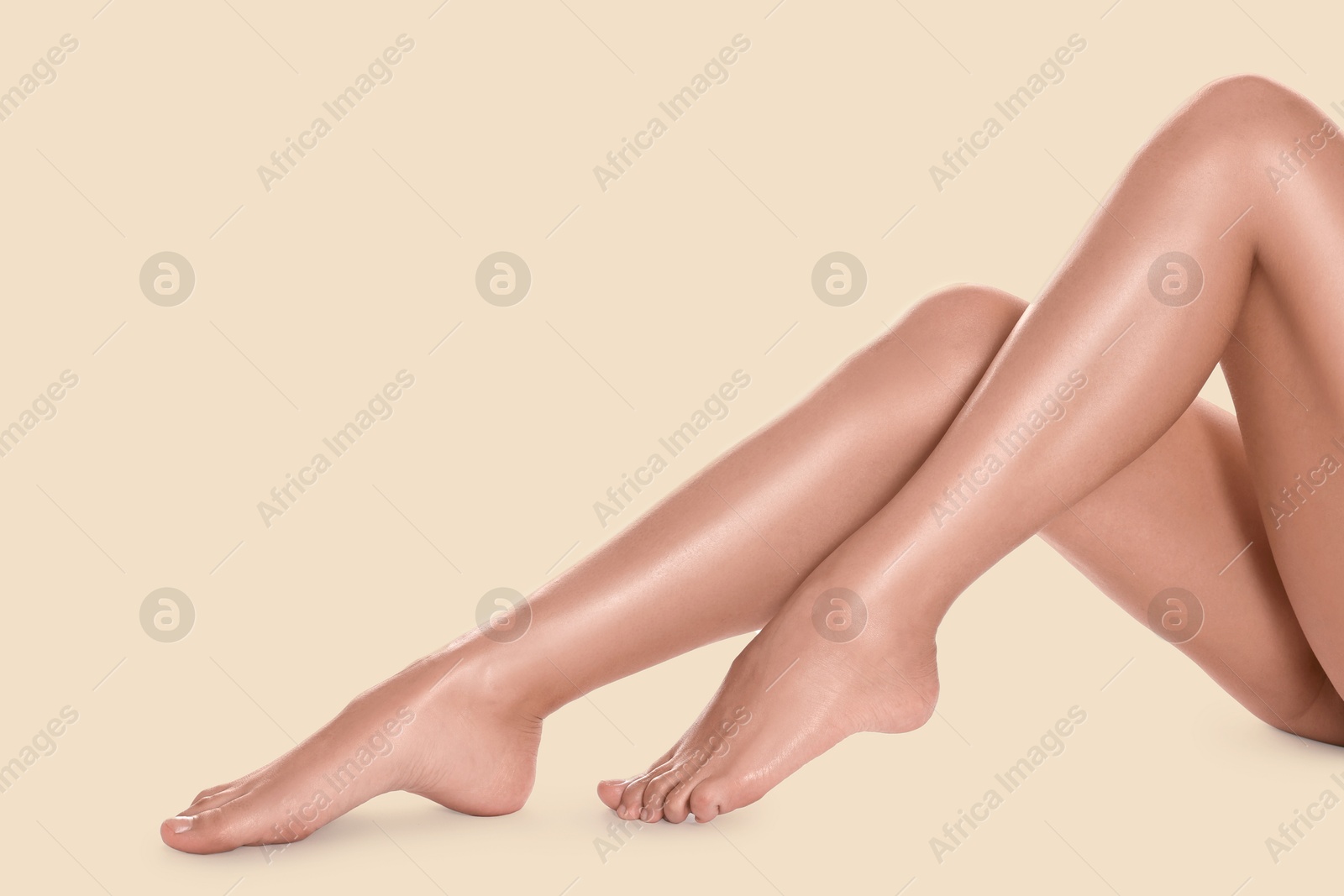 Image of Young woman showing legs with smooth skin after epilation procedure on beige background, closeup