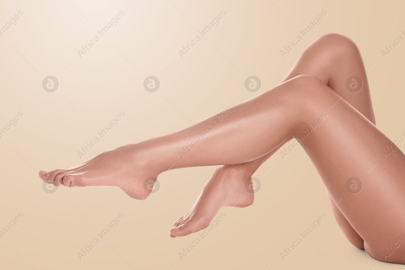 Image of Young woman showing legs with smooth skin after epilation procedure on beige background, closeup