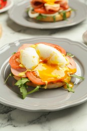 Photo of Tasty brunch. Poached egg, ham, tomato, arugula and bun on white marble table, closeup