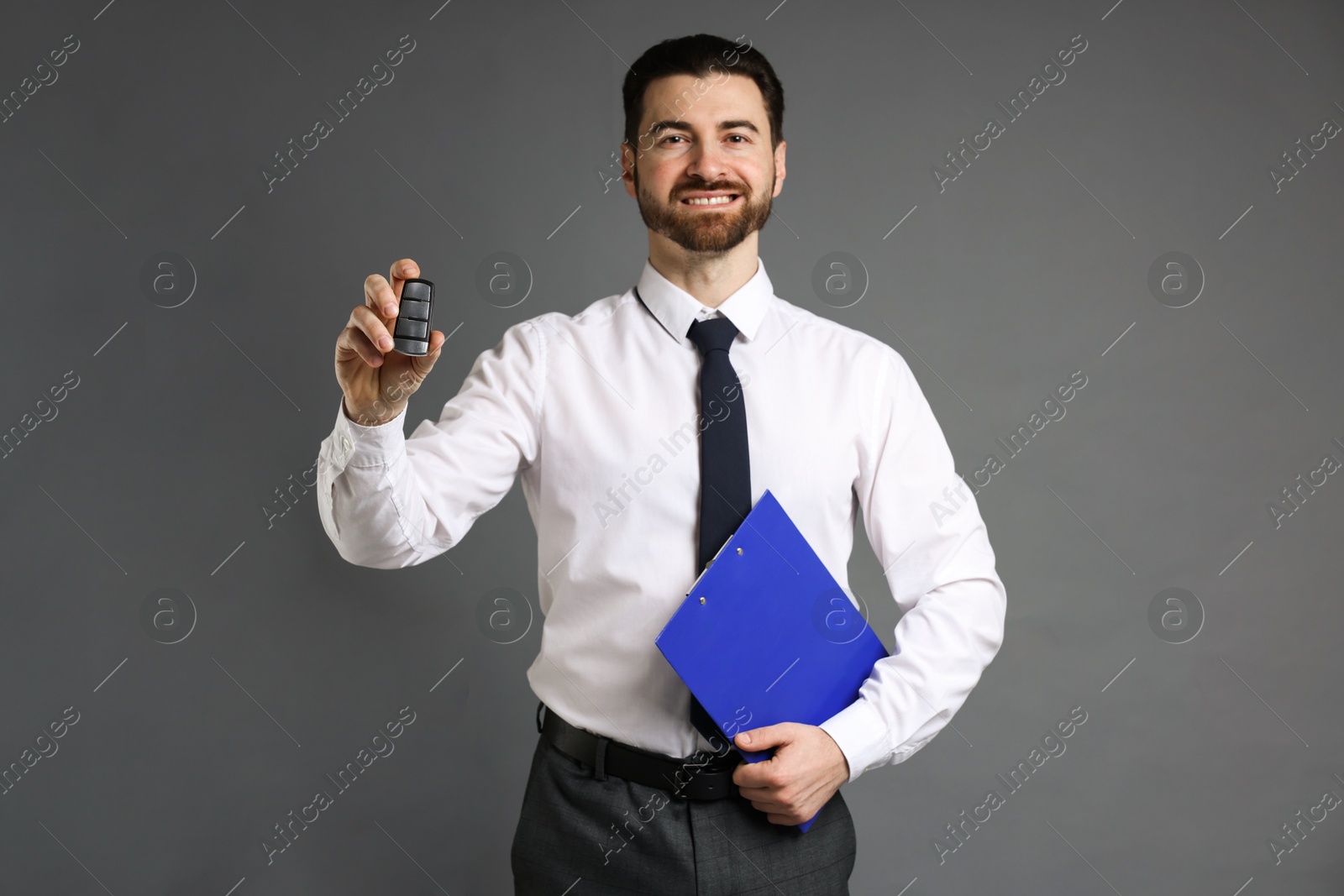 Photo of Cheerful salesman with car key and clipboard on grey background