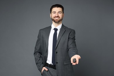 Cheerful salesman with car key on grey background