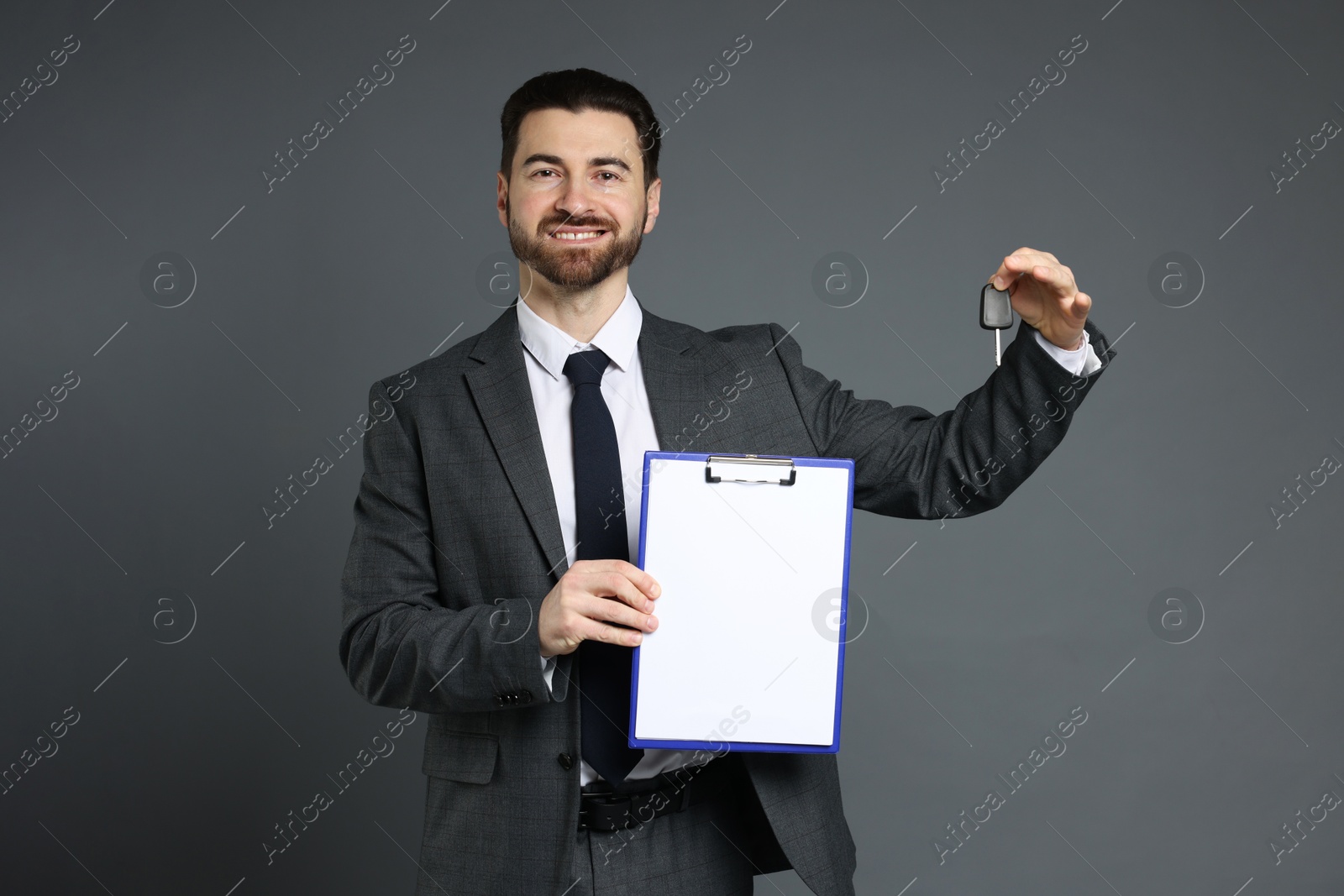 Photo of Cheerful salesman with car key and clipboard on grey background