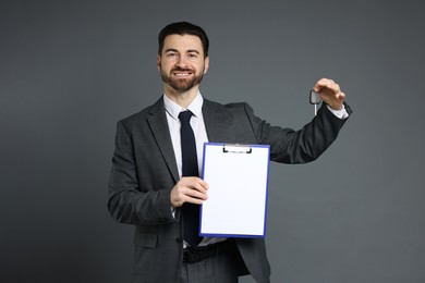 Cheerful salesman with car key and clipboard on grey background