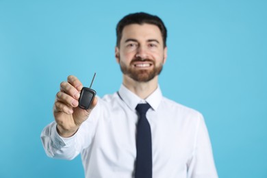 Photo of Cheerful salesman with car key on light blue background, selective focus