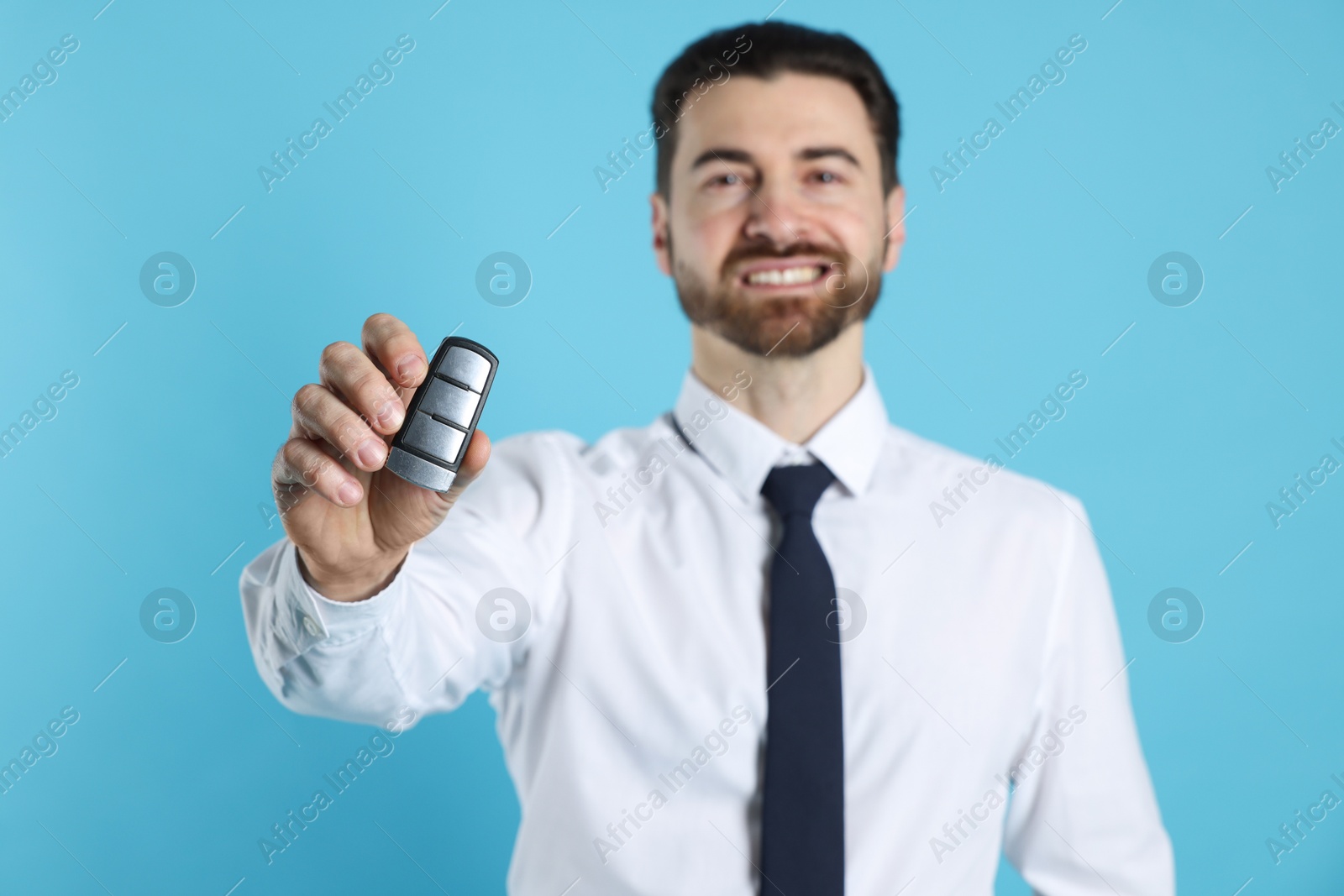 Photo of Cheerful salesman with car key on light blue background, selective focus