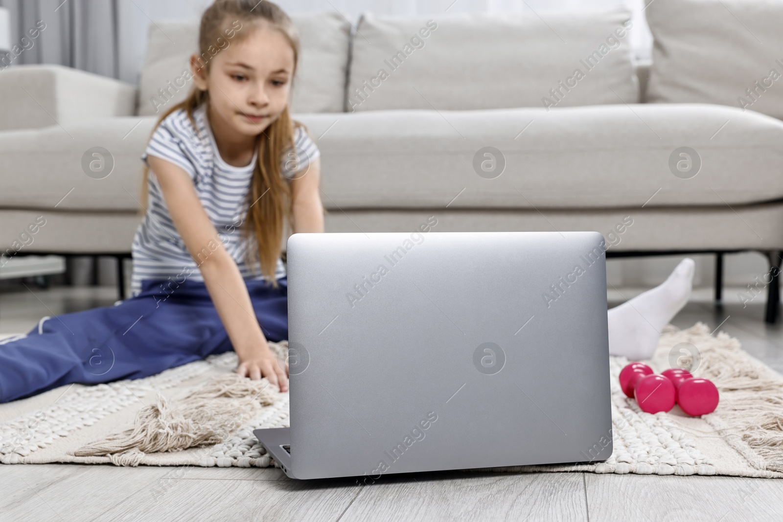 Photo of Little girl exercising near laptop at home, selective focus. Morning routine