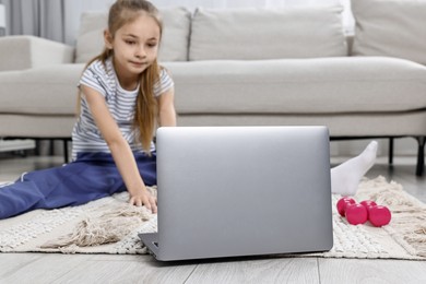 Little girl exercising near laptop at home, selective focus. Morning routine