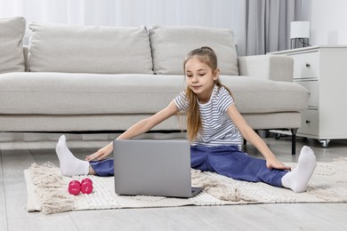 Photo of Little girl exercising near laptop at home. Morning routine