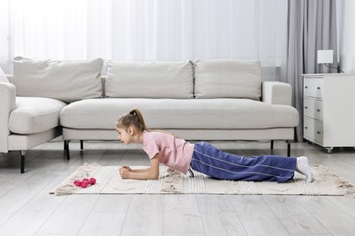 Photo of Little girl doing plank exercise at home. Morning routine