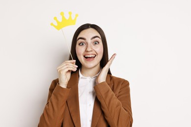 Happy businesswoman holding stick with paper crown on light background