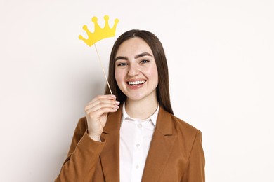 Happy businesswoman holding stick with paper crown on light background