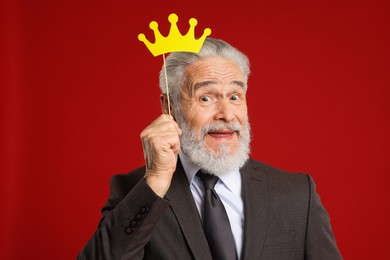 Senior man holding stick with paper crown on red background