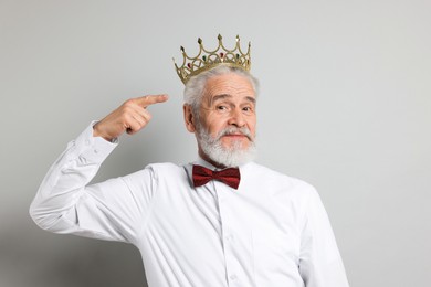 Photo of Senior man pointing at luxury crown on grey background