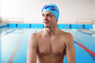 Photo of Young man with cap and goggles near swimming pool indoors