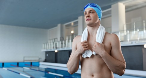 Photo of Young man wearing cap and goggles with towel near swimming pool indoors