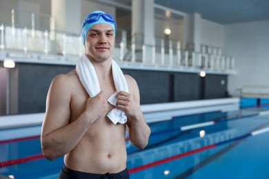 Photo of Young man wearing cap and goggles with towel near swimming pool indoors