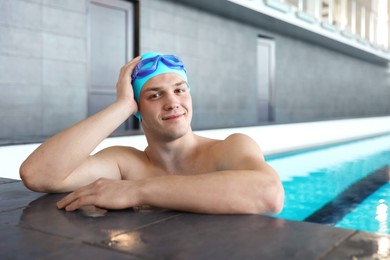 Photo of Young man wearing cap and goggles in swimming pool indoors