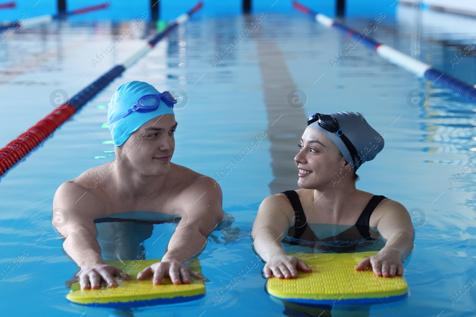 Photo of Young man and woman with kickboards swimming in pool indoors