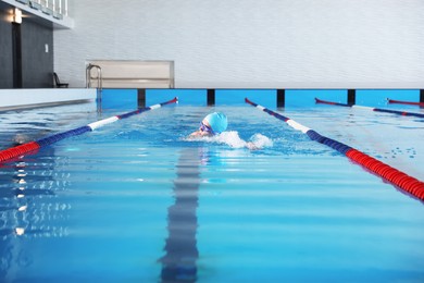 Photo of Young man in cap and goggles swimming in pool indoors