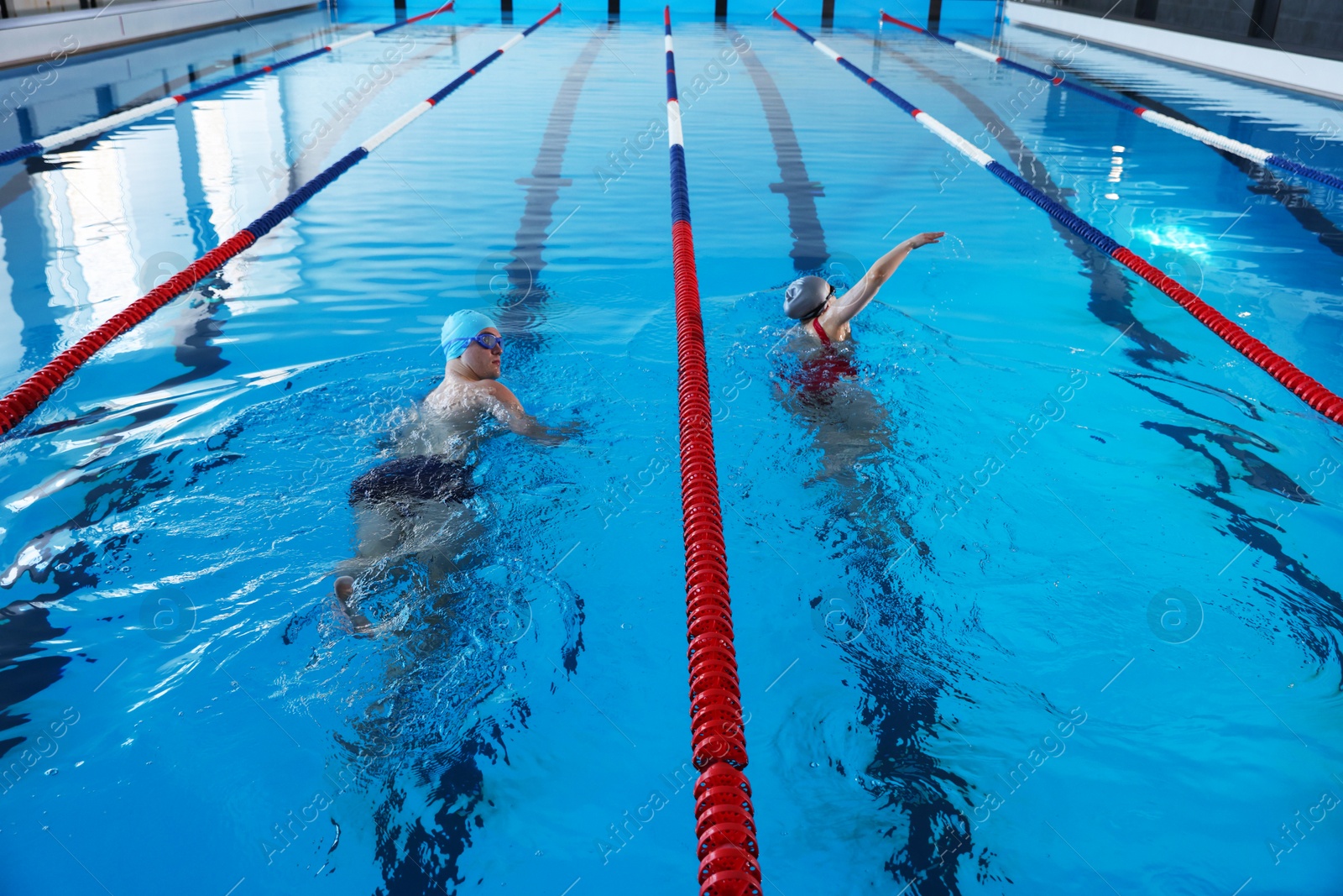 Photo of Young man and woman swimming in pool indoors