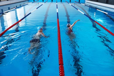 Young man and woman swimming in pool indoors